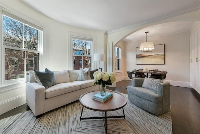 living area featuring crown molding, an inviting chandelier, arched walkways, baseboards, and wood finished floors