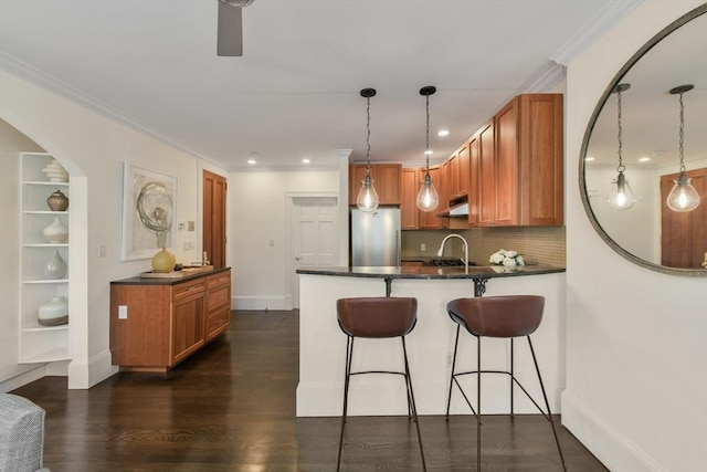 kitchen with a sink, freestanding refrigerator, a peninsula, backsplash, and under cabinet range hood