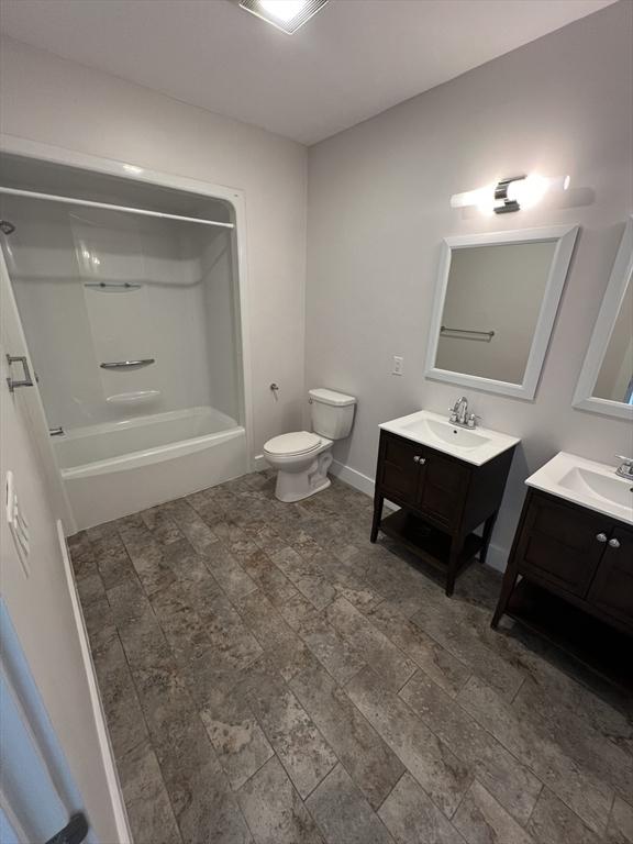 full bathroom featuring baseboards, toilet, two vanities,  shower combination, and a sink