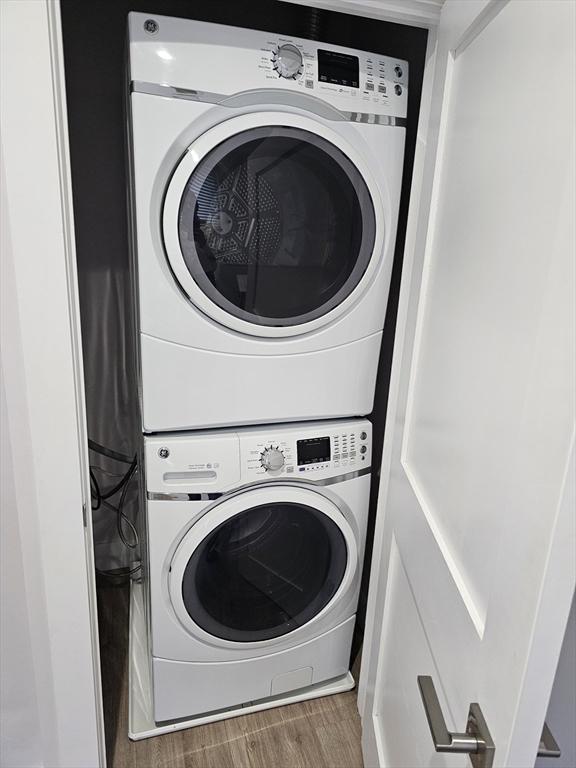 clothes washing area with laundry area, stacked washer and dryer, and wood finished floors