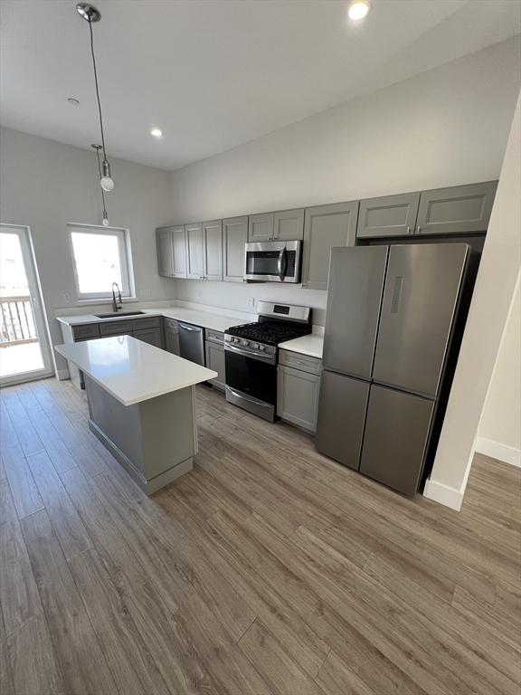 kitchen with gray cabinets, a sink, stainless steel appliances, light countertops, and light wood-style floors