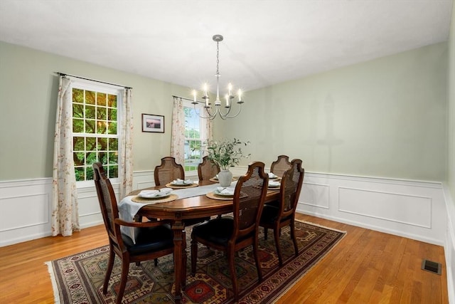 dining area featuring a chandelier, light wood-style floors, a wainscoted wall, and a decorative wall