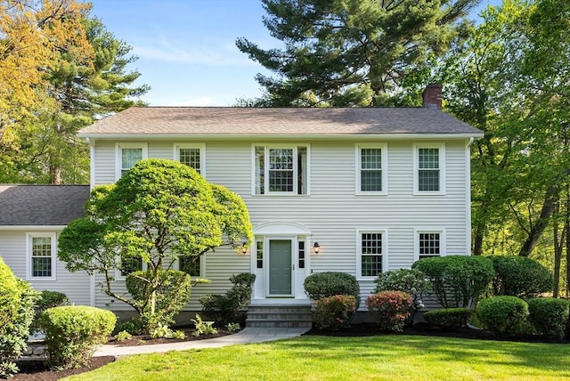 colonial house with a chimney, a front lawn, entry steps, and a shingled roof