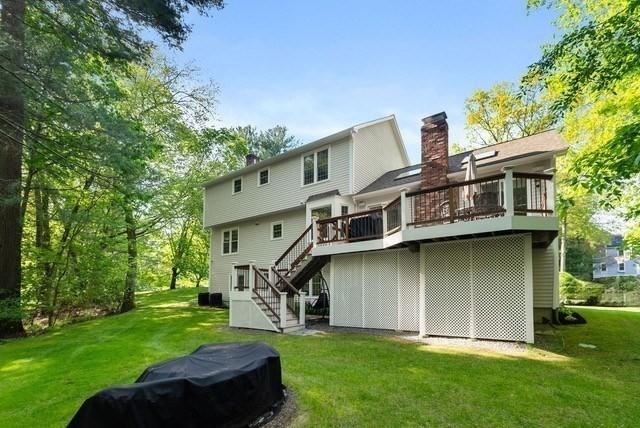 back of house featuring stairway, a chimney, a wooden deck, and a lawn