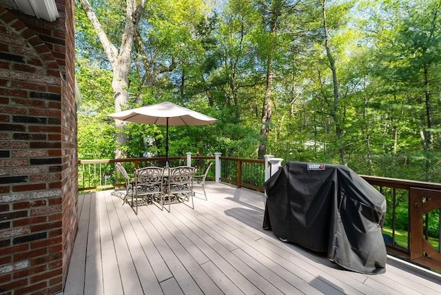 wooden deck with outdoor dining space, a grill, and view of scattered trees