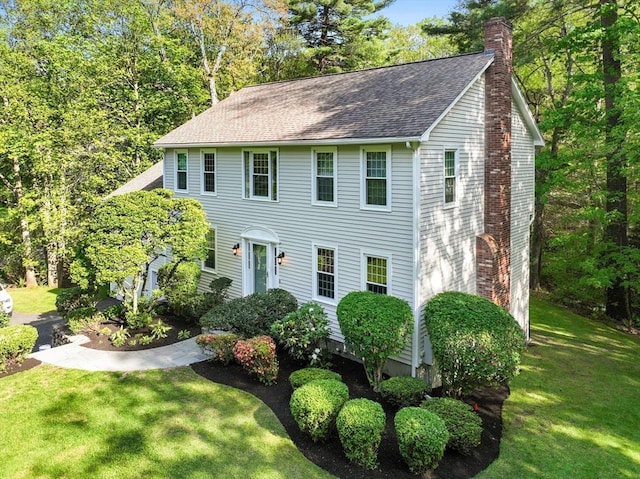 colonial-style house featuring a chimney, a front yard, and a shingled roof
