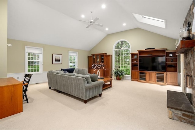 living room featuring carpet, a skylight, a ceiling fan, lofted ceiling, and a fireplace