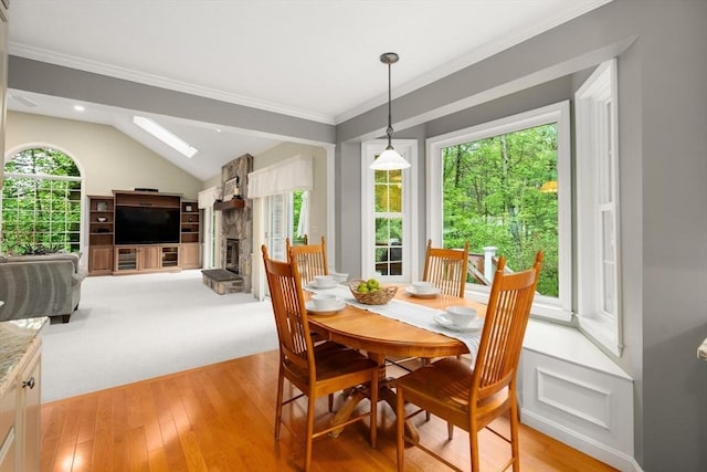 dining area with a fireplace, lofted ceiling, light wood finished floors, and crown molding