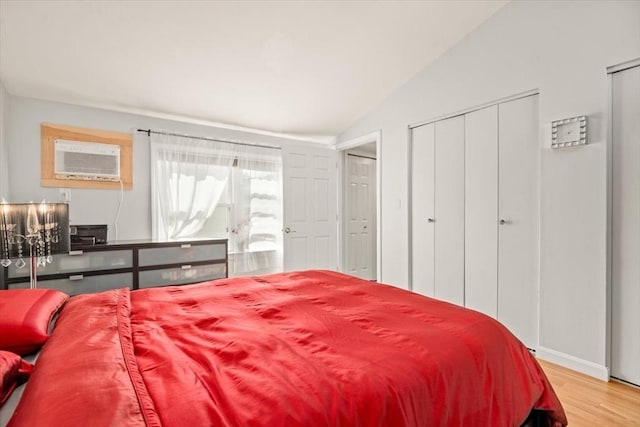 bedroom with wood finished floors, baseboards, lofted ceiling, and an AC wall unit