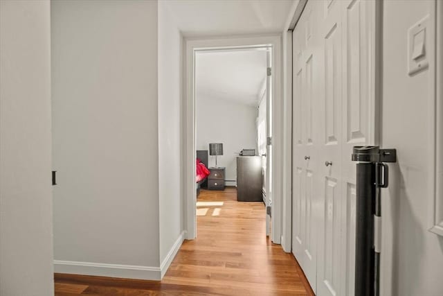 corridor featuring baseboards, baseboard heating, and light wood finished floors