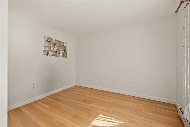 empty room featuring baseboards, a baseboard heating unit, and light wood-style floors