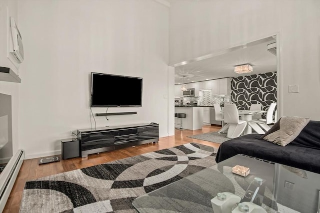 living room with light wood-style floors, a baseboard radiator, baseboards, and a towering ceiling