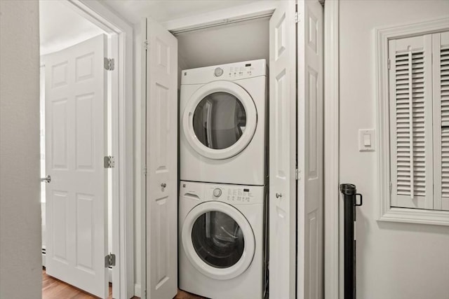clothes washing area with laundry area, stacked washer and clothes dryer, and light wood-type flooring