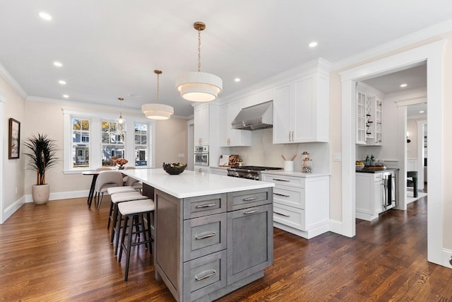 kitchen featuring pendant lighting, a kitchen island, white cabinets, wall chimney range hood, and dark wood-type flooring