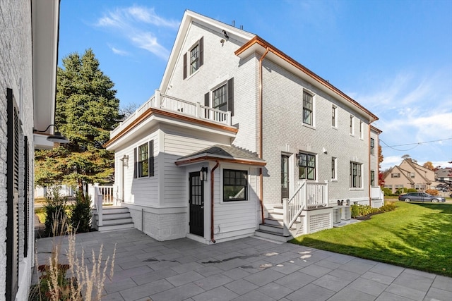 rear view of house with a balcony, a lawn, and a patio