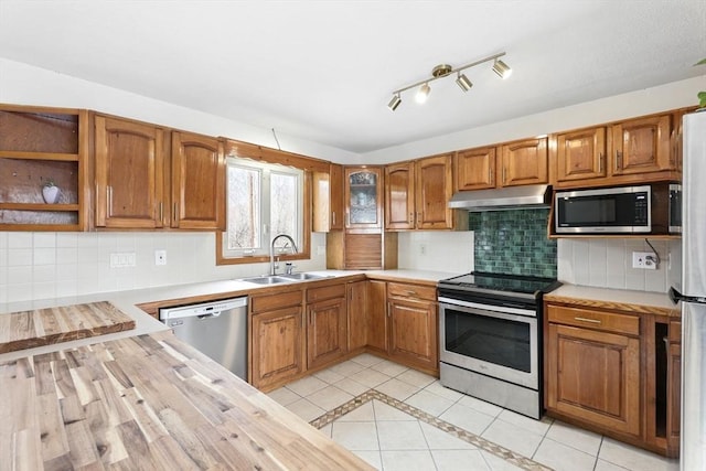 kitchen featuring light tile patterned flooring, a sink, brown cabinetry, stainless steel appliances, and under cabinet range hood