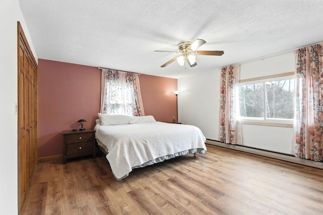 bedroom featuring a textured ceiling, a baseboard heating unit, multiple windows, and wood finished floors