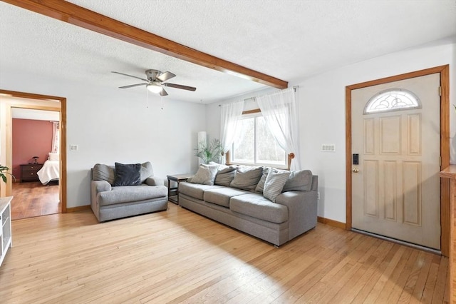 living area with a healthy amount of sunlight, ceiling fan, light wood-type flooring, and beam ceiling