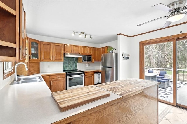 kitchen featuring brown cabinetry, decorative backsplash, under cabinet range hood, a sink, and appliances with stainless steel finishes