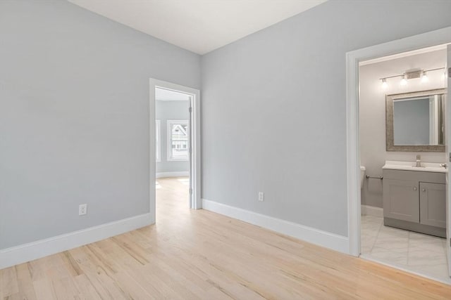 unfurnished bedroom featuring ensuite bathroom, sink, and light hardwood / wood-style floors