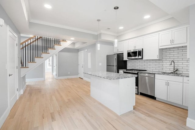 kitchen with sink, decorative light fixtures, appliances with stainless steel finishes, a kitchen island, and white cabinets