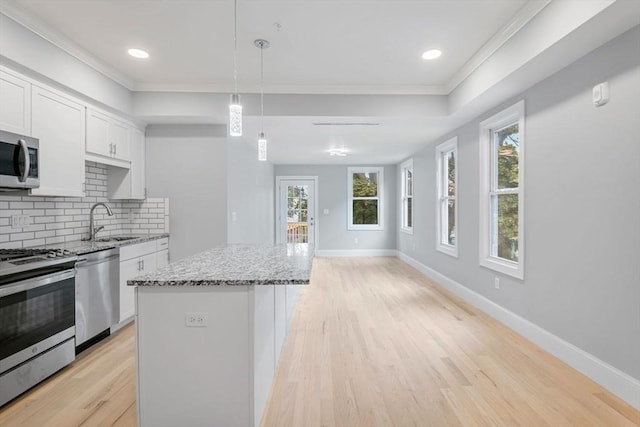 kitchen featuring a kitchen island, white cabinetry, hanging light fixtures, stainless steel appliances, and light stone countertops