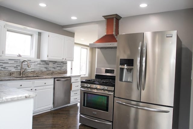 kitchen featuring stainless steel appliances, a sink, wall chimney exhaust hood, white cabinetry, and light stone countertops