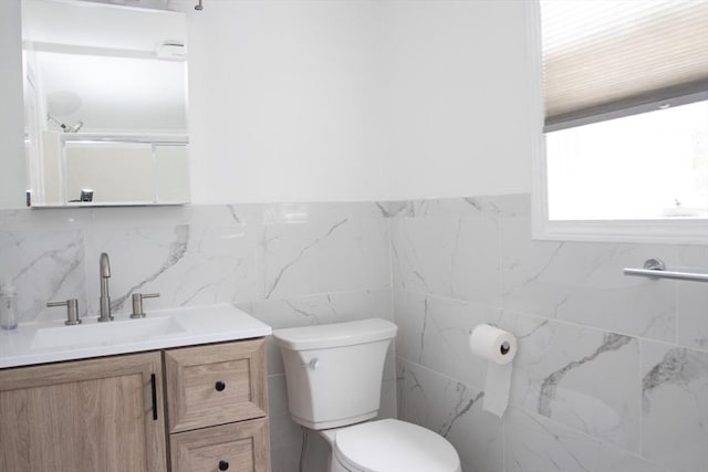 bathroom featuring toilet, vanity, and tile walls