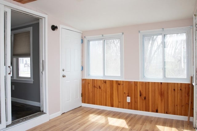 entryway with light wood finished floors, wainscoting, healthy amount of natural light, wood walls, and lofted ceiling
