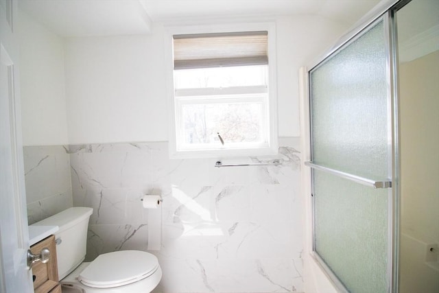 bathroom with a shower with shower door, toilet, tile walls, and wainscoting