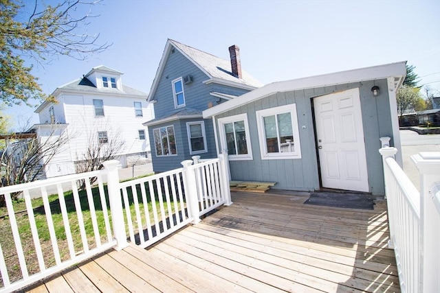 back of house with a wooden deck, a chimney, and board and batten siding