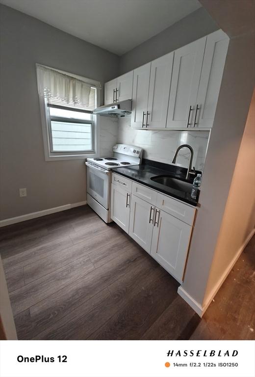 54 Shirley Ave, Revere, MA 02151 - kitchen with white electric range, a sink, dark countertops, under cabinet range hood, and dark wood-style flooring