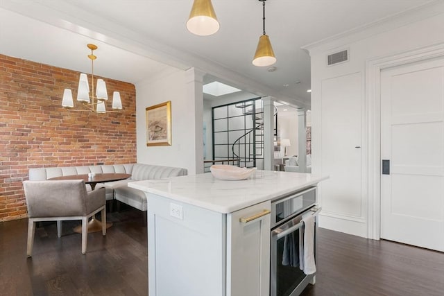 kitchen featuring hanging light fixtures, crown molding, oven, and brick wall