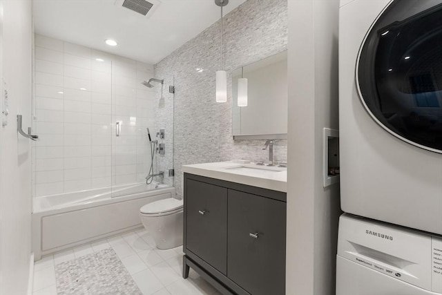 full bathroom with stacked washer and dryer, toilet, shower / bath combination with glass door, tile walls, and vanity