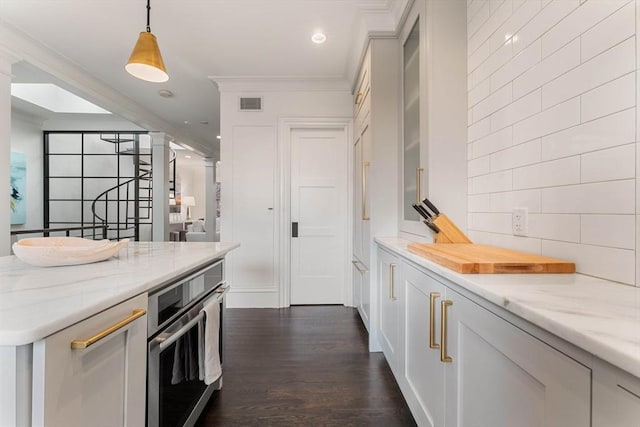 kitchen with dark wood-type flooring, hanging light fixtures, ornamental molding, light stone countertops, and oven