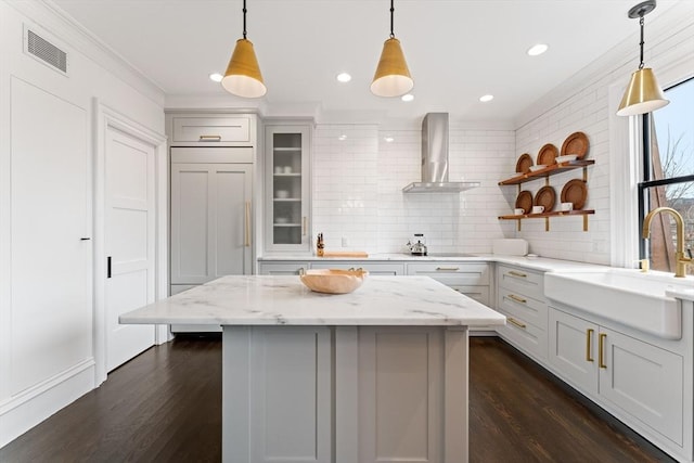 kitchen featuring tasteful backsplash, paneled built in refrigerator, pendant lighting, light stone countertops, and wall chimney range hood