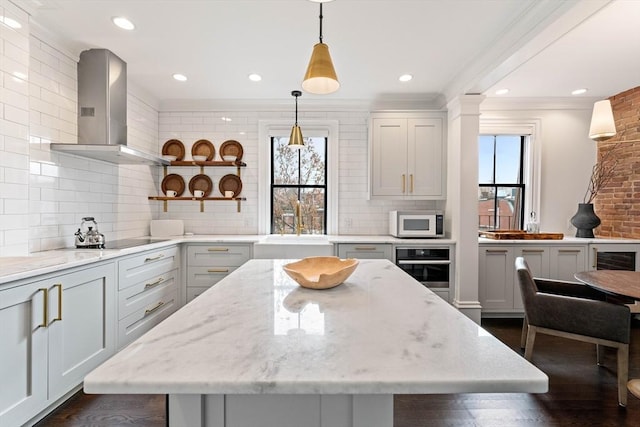 kitchen with hanging light fixtures, black electric cooktop, light stone counters, and wall chimney exhaust hood