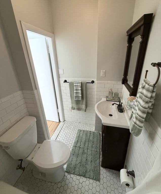 bathroom featuring tile walls, a wainscoted wall, tile patterned floors, toilet, and vanity