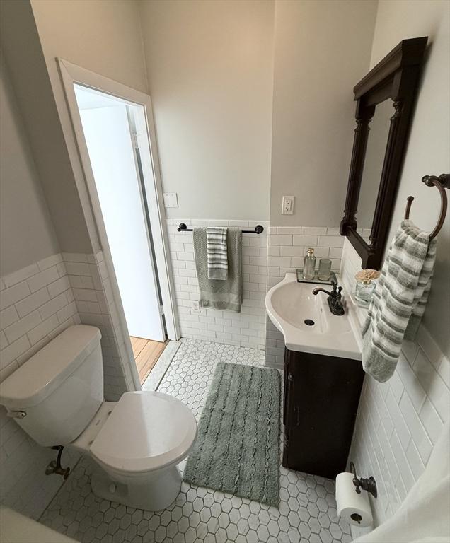 bathroom featuring tile walls, a wainscoted wall, tile patterned floors, toilet, and vanity