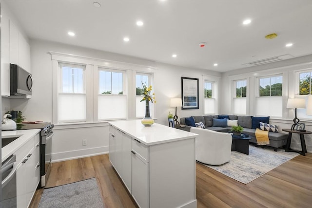 kitchen featuring stainless steel appliances, white cabinetry, a kitchen island, and hardwood / wood-style flooring