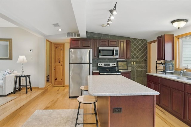kitchen featuring appliances with stainless steel finishes, a breakfast bar, a sink, light countertops, and light wood-style flooring