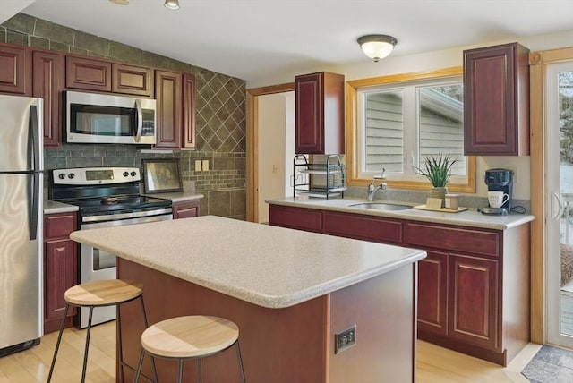 kitchen featuring stainless steel appliances, dark brown cabinets, a sink, a kitchen island, and light countertops
