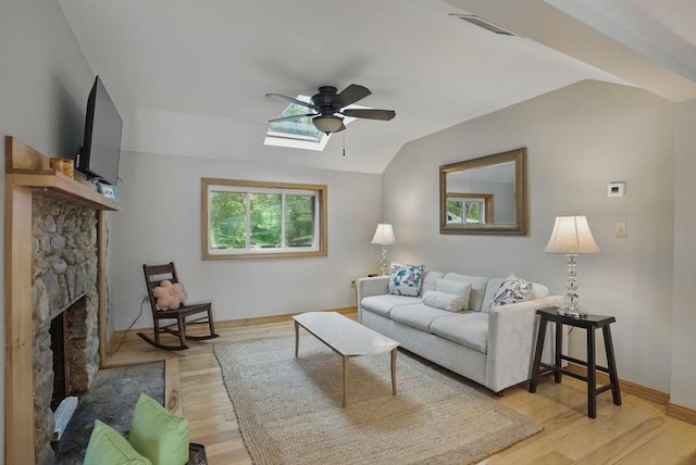 living room with a ceiling fan, light wood-type flooring, a fireplace, vaulted ceiling, and a skylight