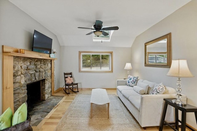 living room featuring a ceiling fan, a stone fireplace, wood finished floors, lofted ceiling, and baseboards