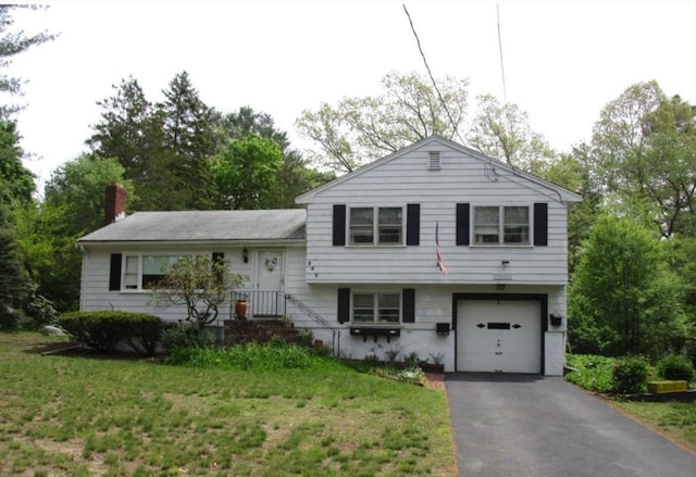 split level home with a front yard, a chimney, a garage, and aphalt driveway