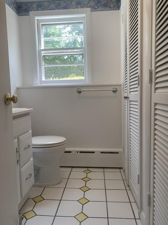 bathroom with toilet, a closet, vanity, tile patterned flooring, and baseboard heating