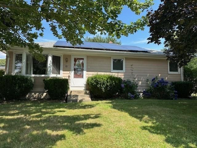 single story home featuring a front lawn and solar panels