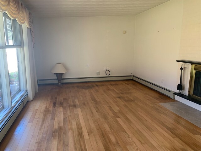 empty room with hardwood / wood-style floors, a baseboard radiator, and a healthy amount of sunlight