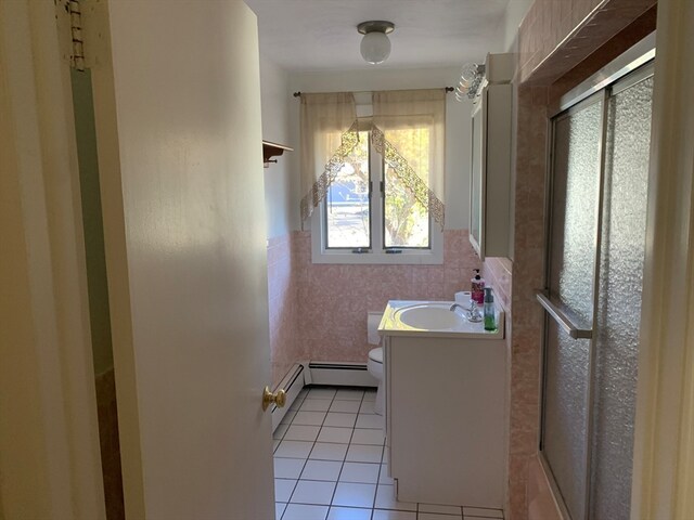 bathroom featuring baseboard heating, tile patterned flooring, toilet, vanity, and tile walls