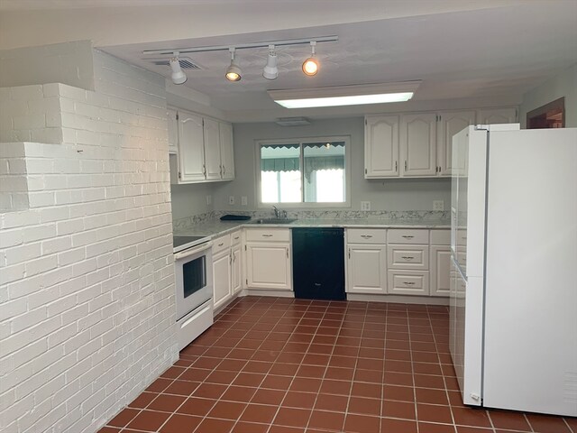 kitchen featuring white appliances, rail lighting, dark tile patterned floors, white cabinetry, and brick wall